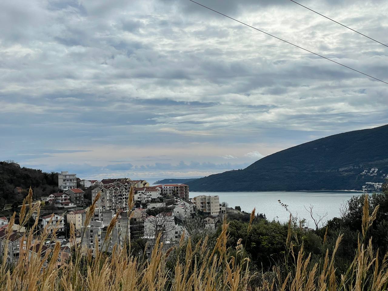 Панорамный вид на море и город Герцег-Нови, Черногория, с земельного участка №1519 на фоне гор и облачного неба.