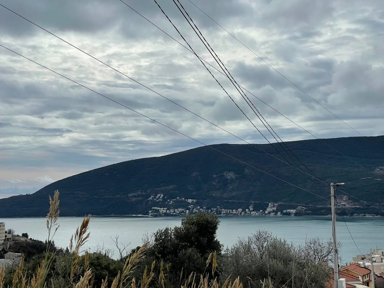 Scenic view of the sea and a mountainous coastline with a village under cloudy skies.