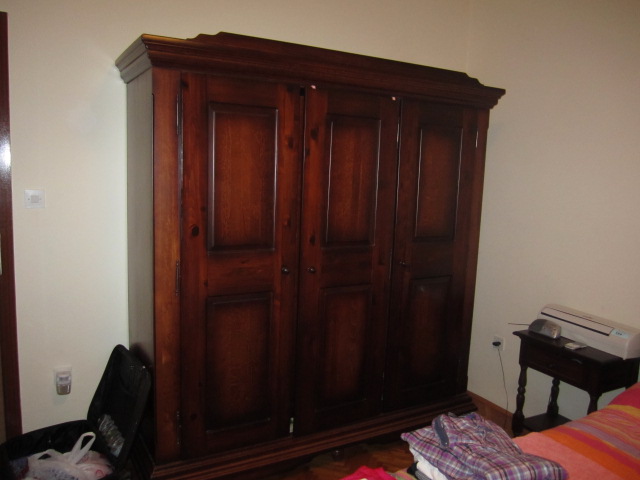 A large wooden wardrobe in the bedroom of a house in Tivat, Montenegro. Nearby are a bedside table and an air conditioner.