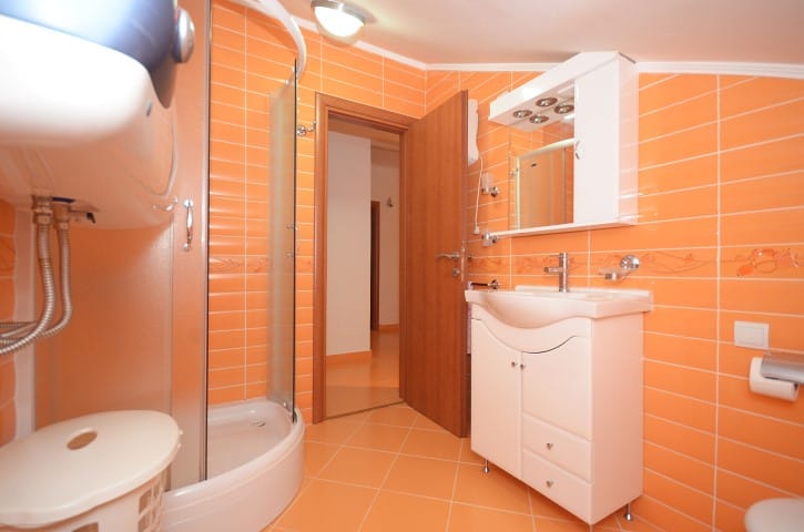 Bathroom with orange tiles, a shower cabin, and white furniture in a house, Krašići, Montenegro.