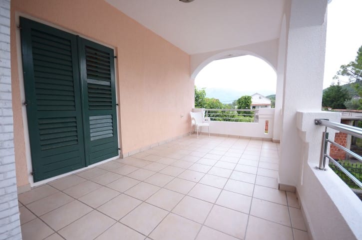 Spacious terrace with tile and green shutters in a house, Krašići, Montenegro: mountain and garden view from the balcony.