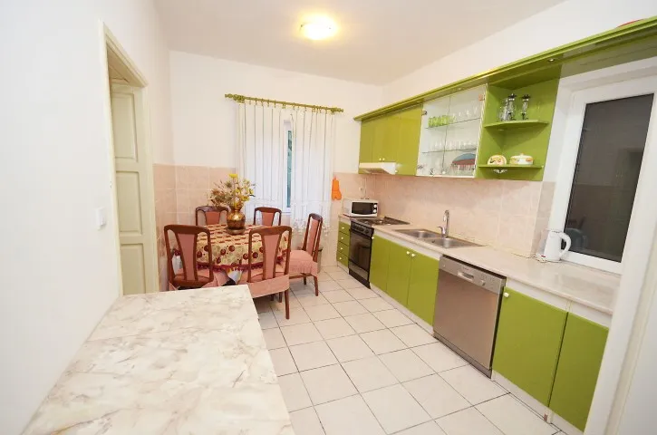 Kitchen with green cabinets, dining table set, stove, sink, and dishwasher on white tiled flooring.