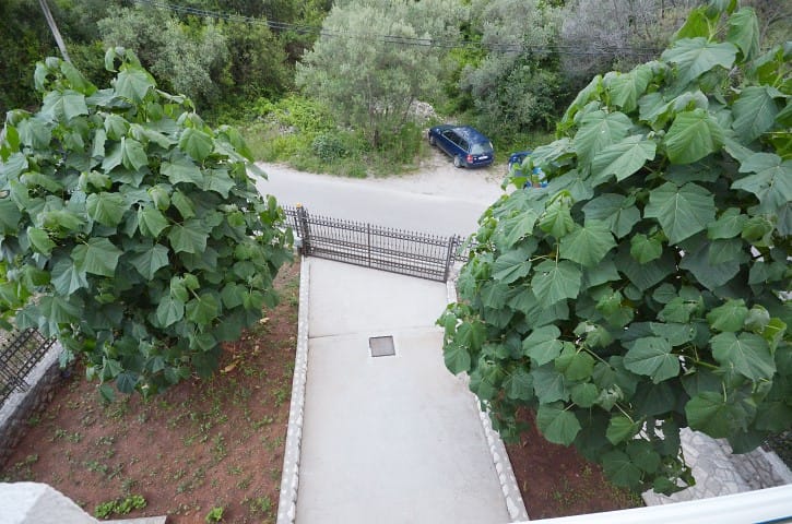 Top view of a private parking area and the house’s entrance gate in Krašići, Montenegro, surrounded by green trees.