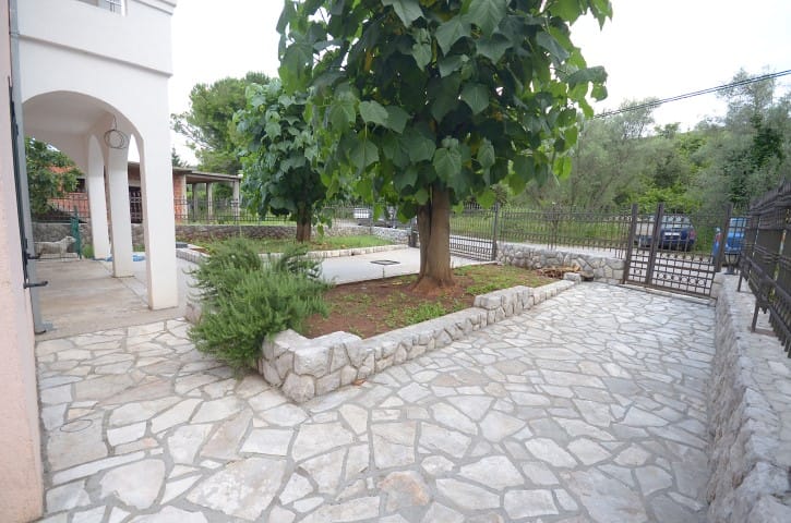 Cozy house courtyard in Krašići, Montenegro: a stone-paved area, green trees, and an arched terrace.