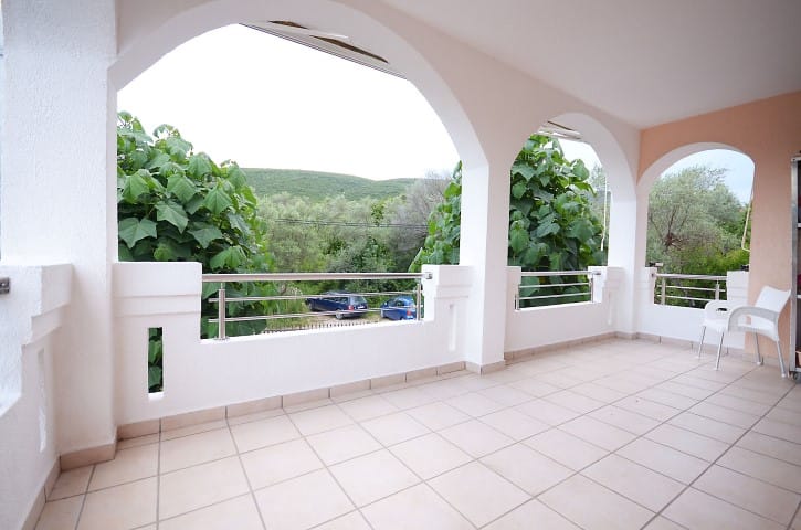 Terrace with arched openings, white walls, tiled floor, metal railing, and a view of green hills and trees.