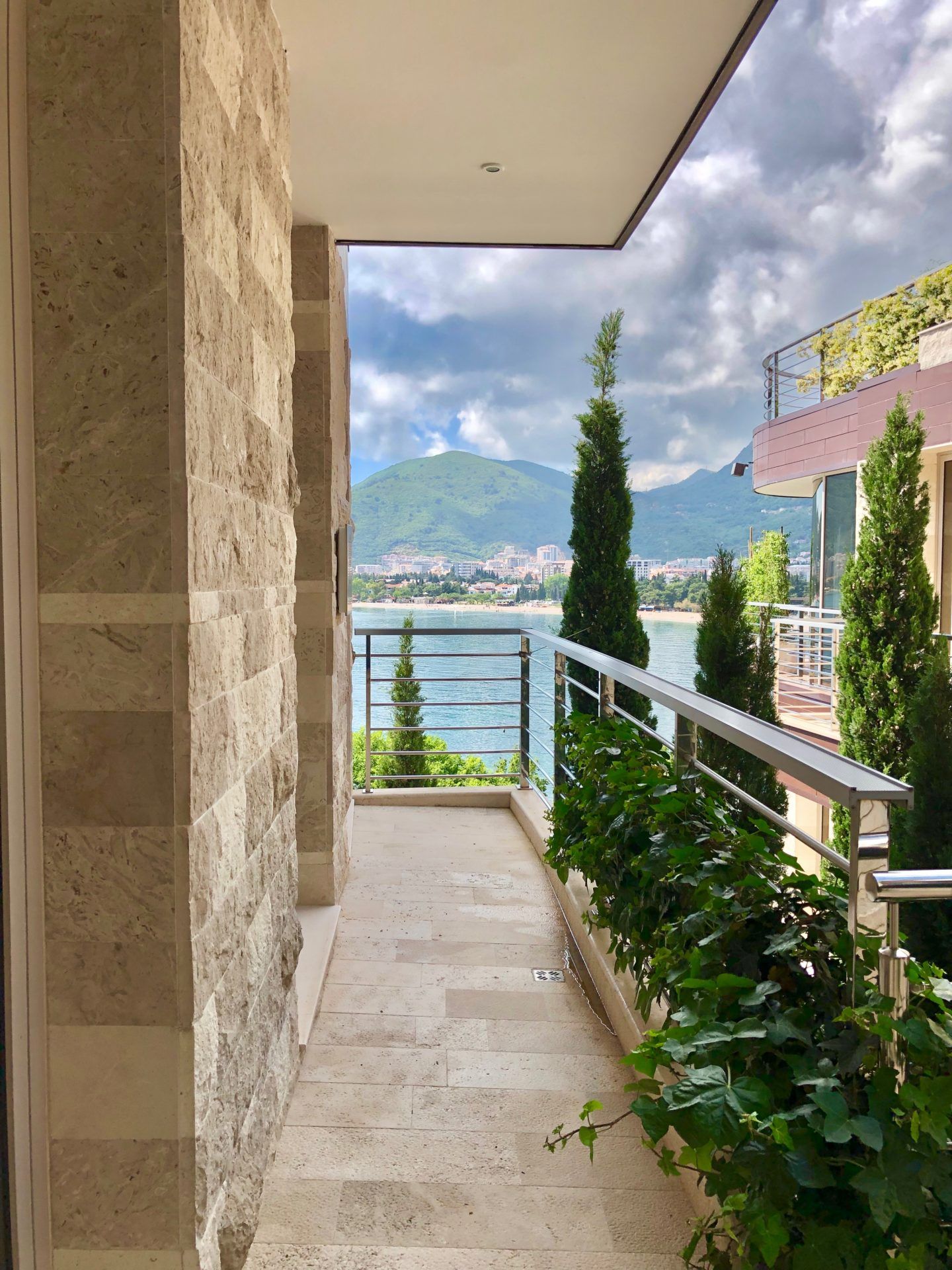 Apartment balcony in Budva, Montenegro: stone finishes, sea and mountain views, greenery, and modern railing.