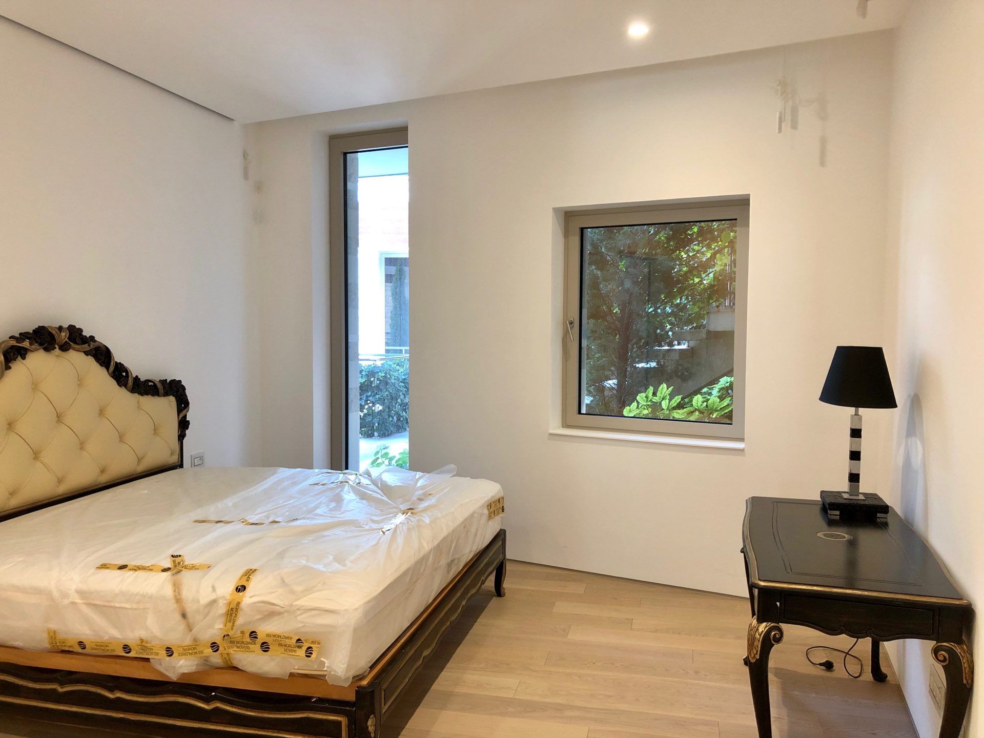 Bedroom in an apartment in Budva, Montenegro: a classic bed, black vanity table, light flooring, and a view of the garden.