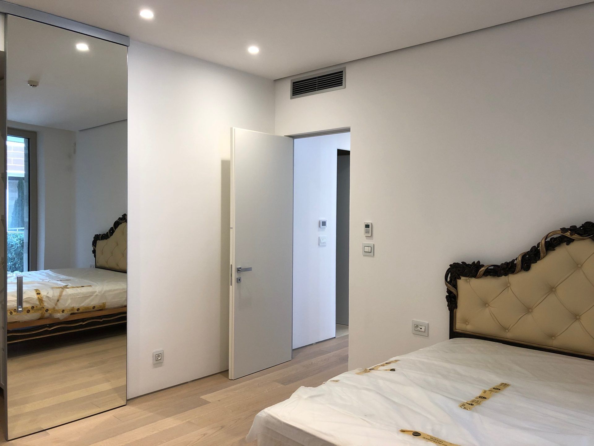 Modern bedroom in an apartment in Budva, Montenegro: a bed with a classic headboard, mirrored wardrobe, and parquet flooring.