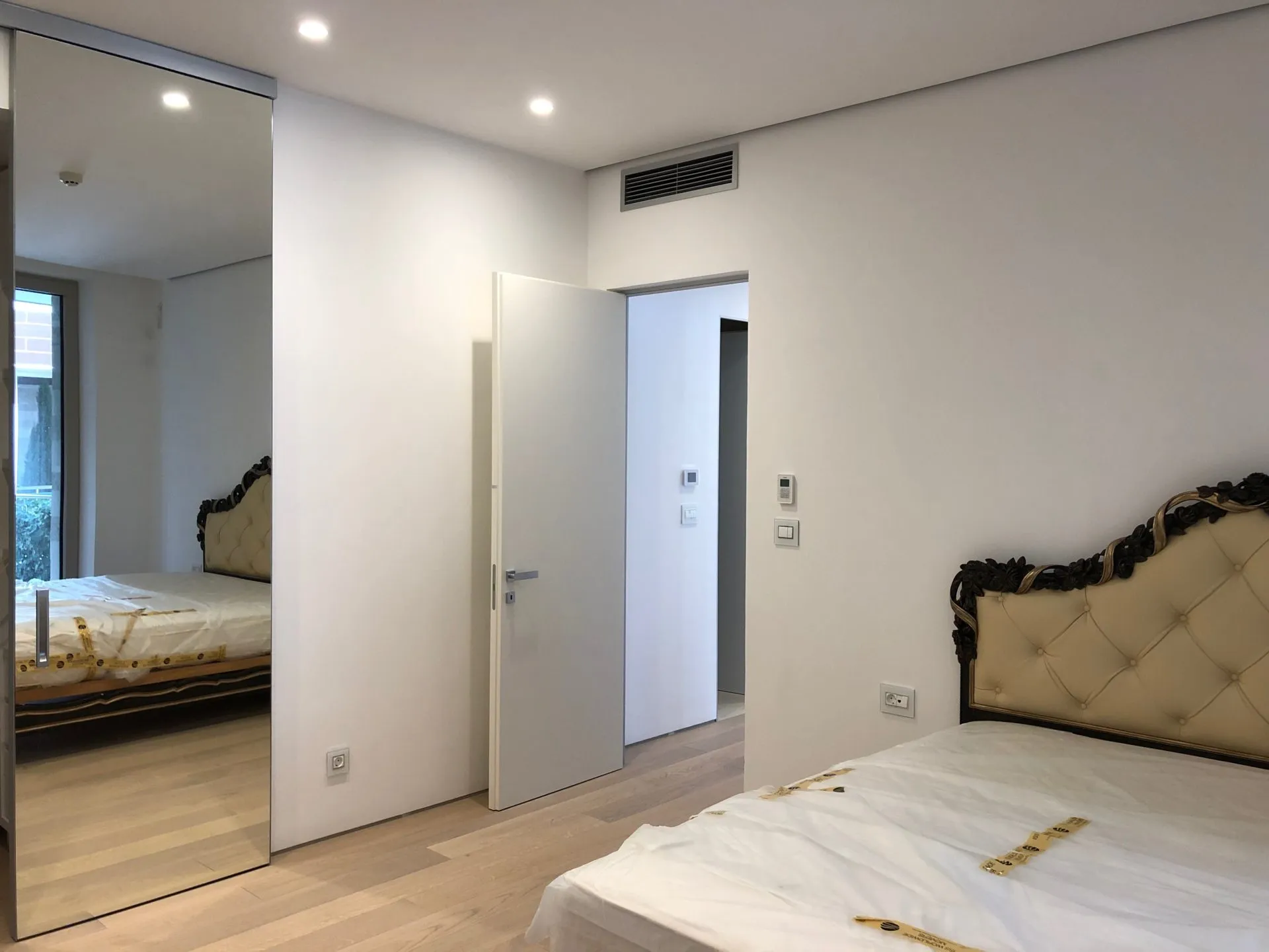 Modern bedroom featuring a bed with white protective cover and a large floor-to-ceiling mirror.