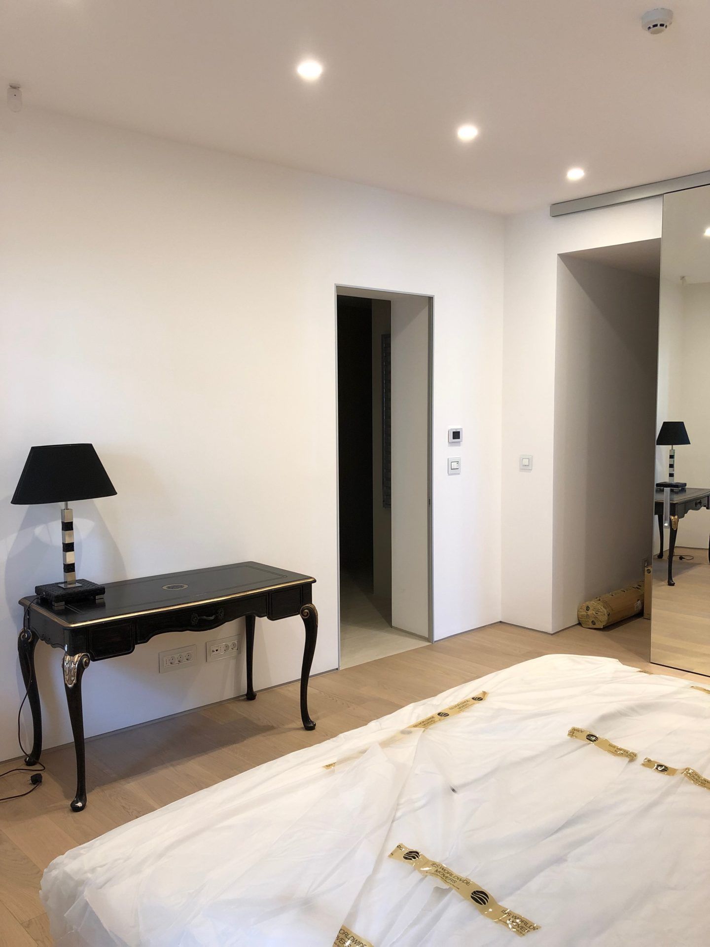 Modern bedroom in an apartment in Budva, Montenegro: vintage console table, black lamp, and mirrored wardrobe.
