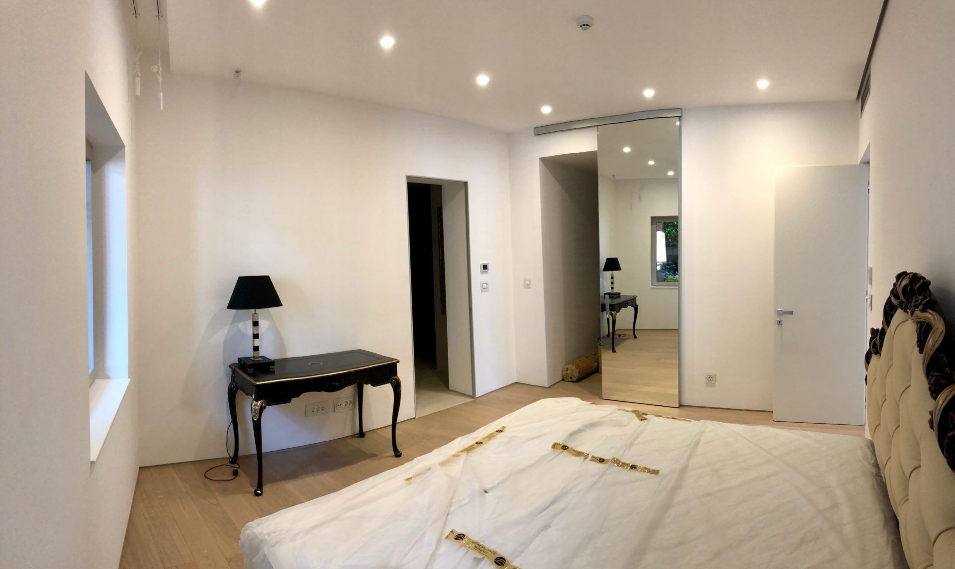 Modern bedroom in an apartment in Budva, Montenegro: double bed, vintage side table, mirror, and recessed lighting.