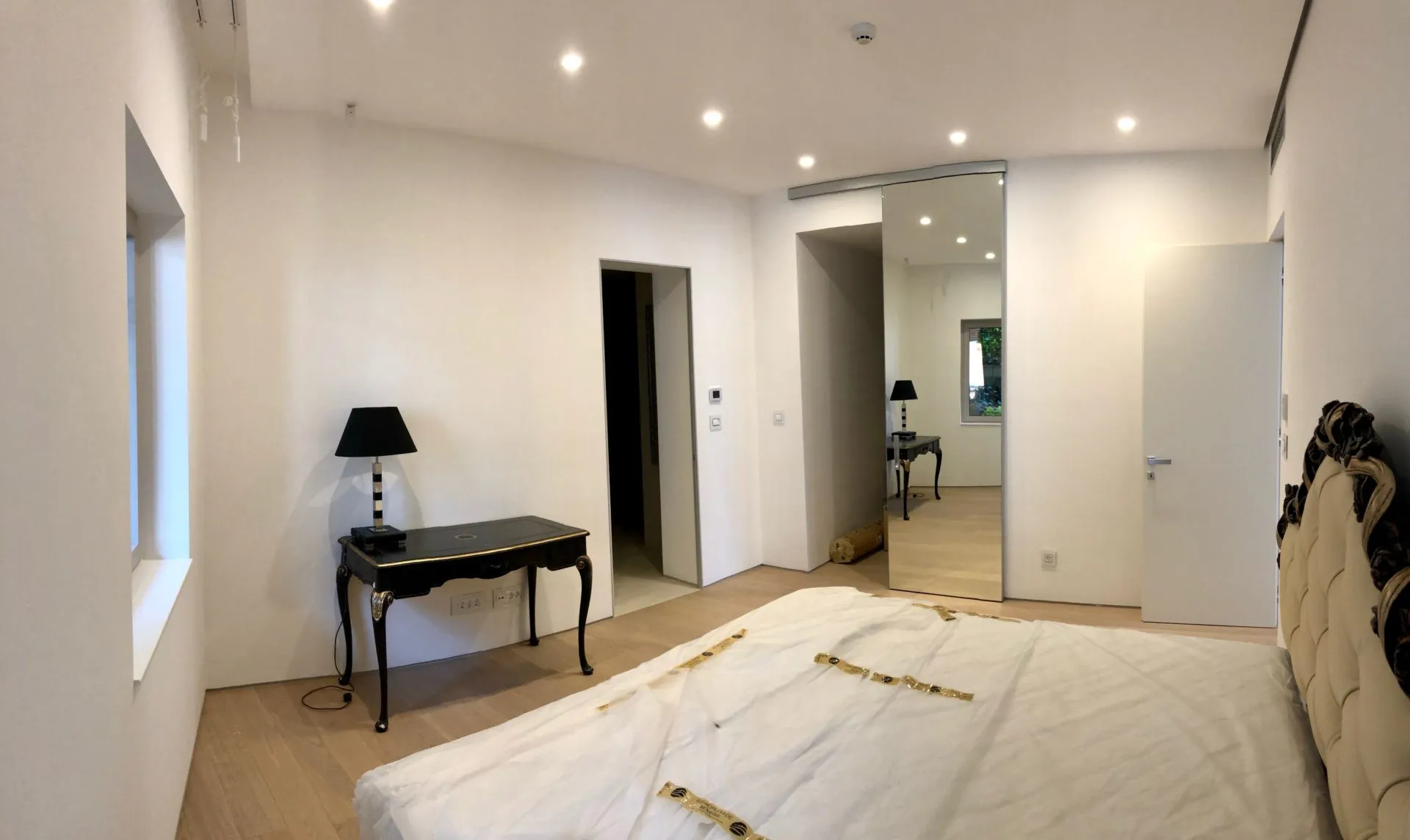 Bright bedroom featuring a large bed with white bedding, a black console table, and a sliding mirror door.