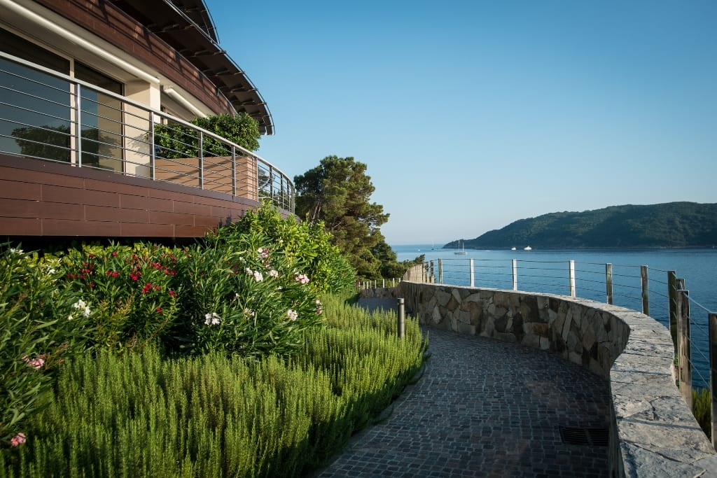 Modern villa in Budva, Montenegro: terrace with sea view, stone pathway, and landscaped garden with flowers.