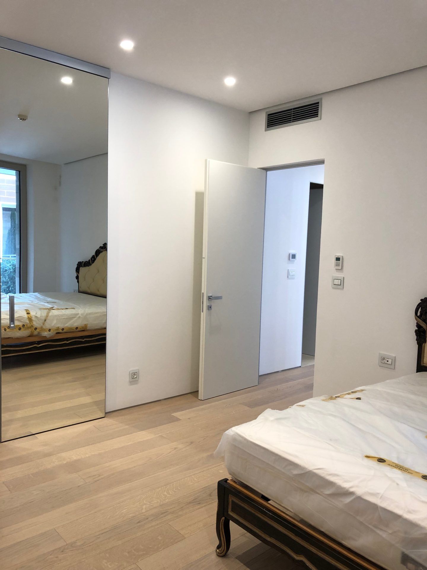 Modern bedroom in an apartment in Budva, Montenegro: bed, mirrored wardrobe, light parquet flooring, and built-in air conditioner.