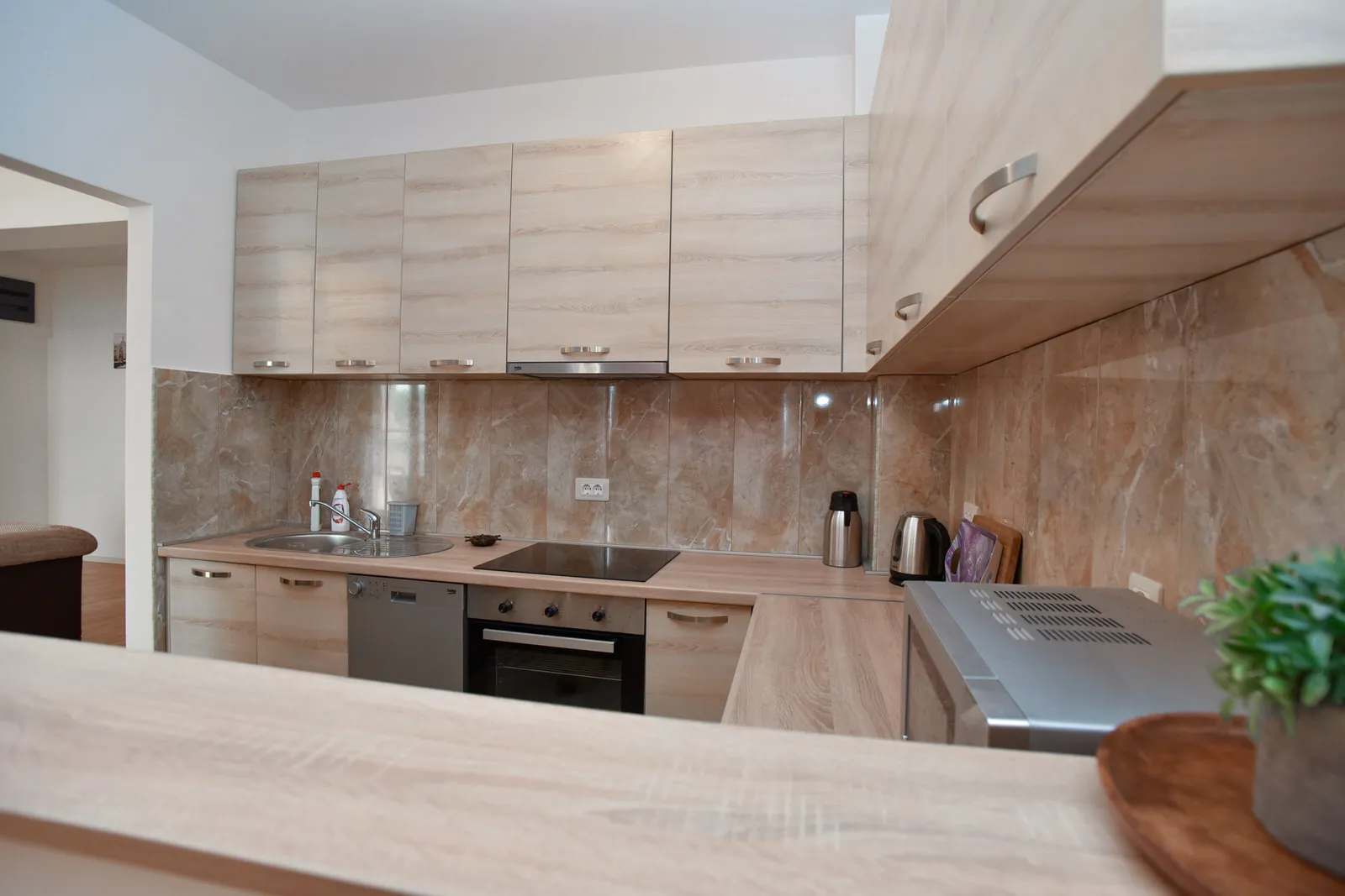 Modern kitchen with light wood cabinets, marble backsplash, sink, induction cooktop, oven, and dishwasher visible.