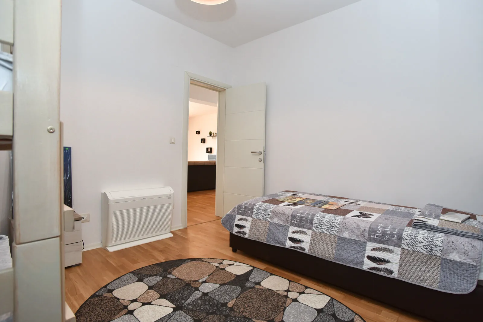 Bedroom featuring a bed with patchwork coverlet, round patterned rug, and wall-mounted heater.