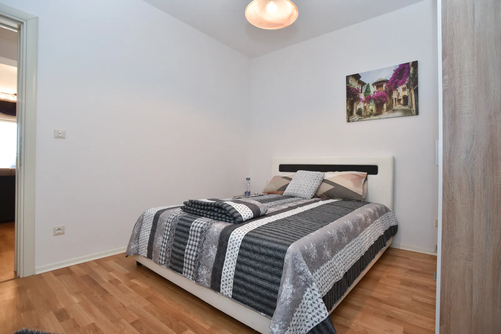 Bedroom featuring a double bed with grey patterned cover, wooden flooring, and wall art above the headboard.