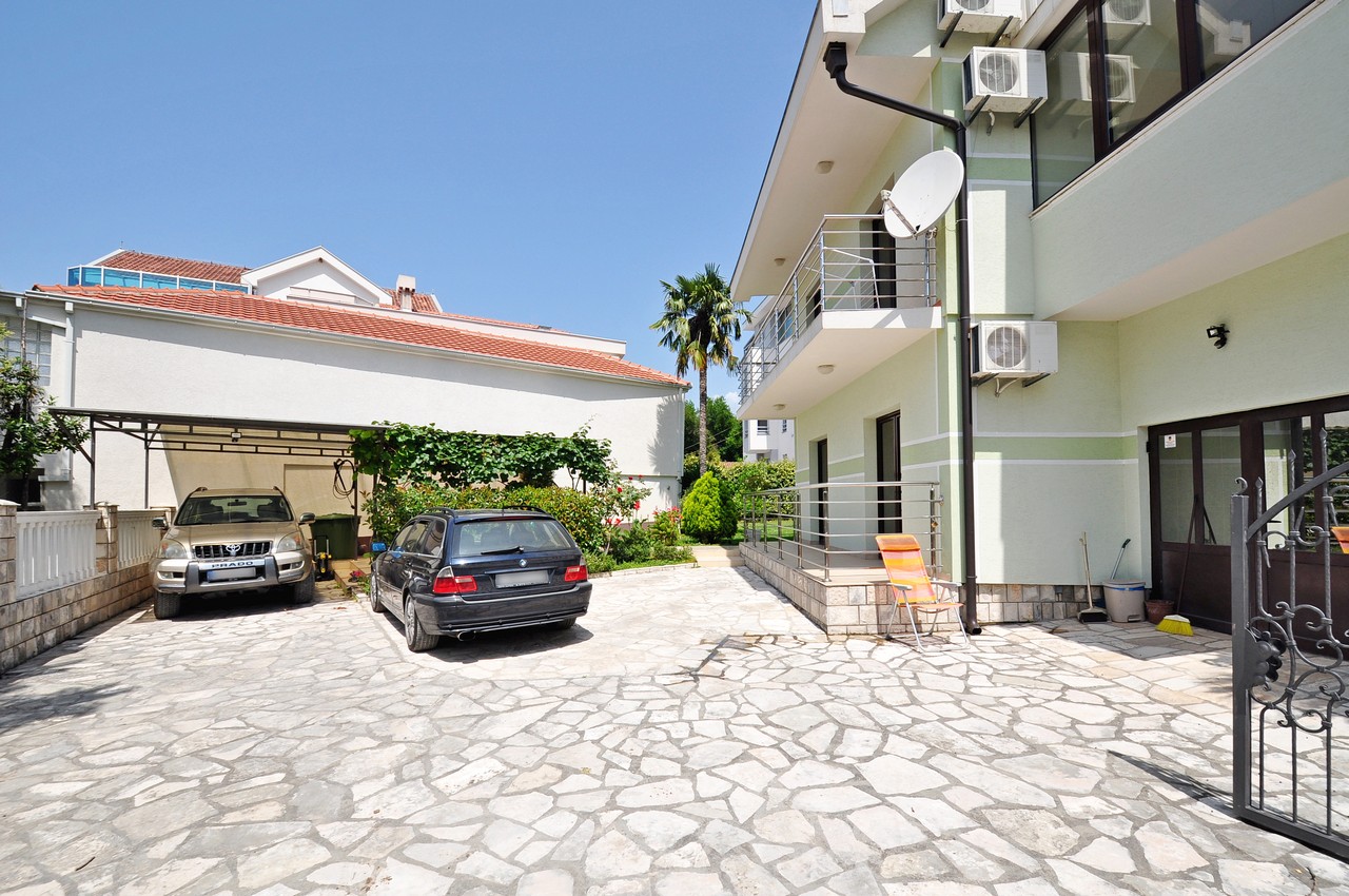 House courtyard in Tivat, Montenegro: parking for two cars, paved area, balcony, and green space.