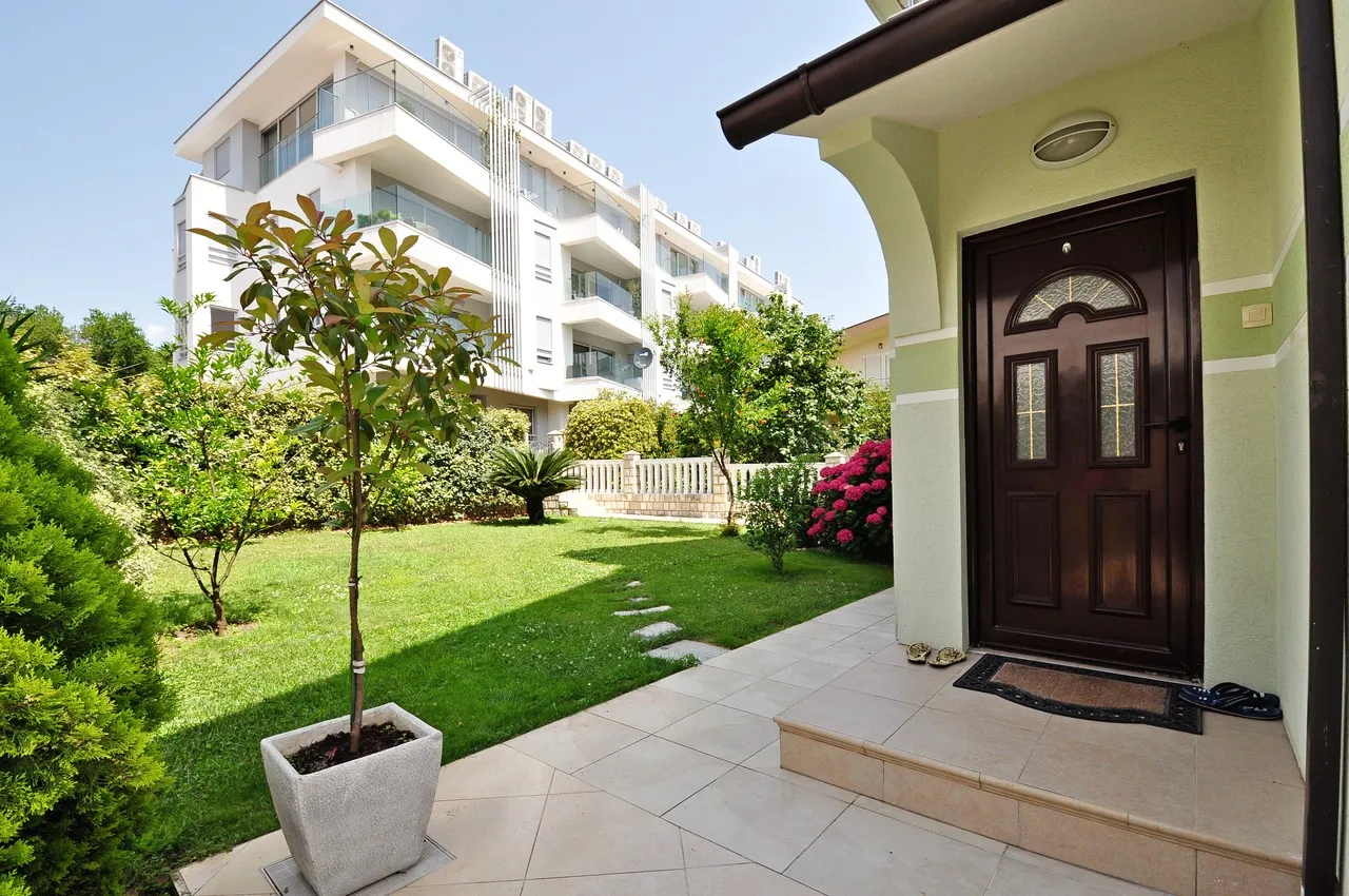 Front entrance door with tiled patio and green lawn garden set against a modern apartment building.