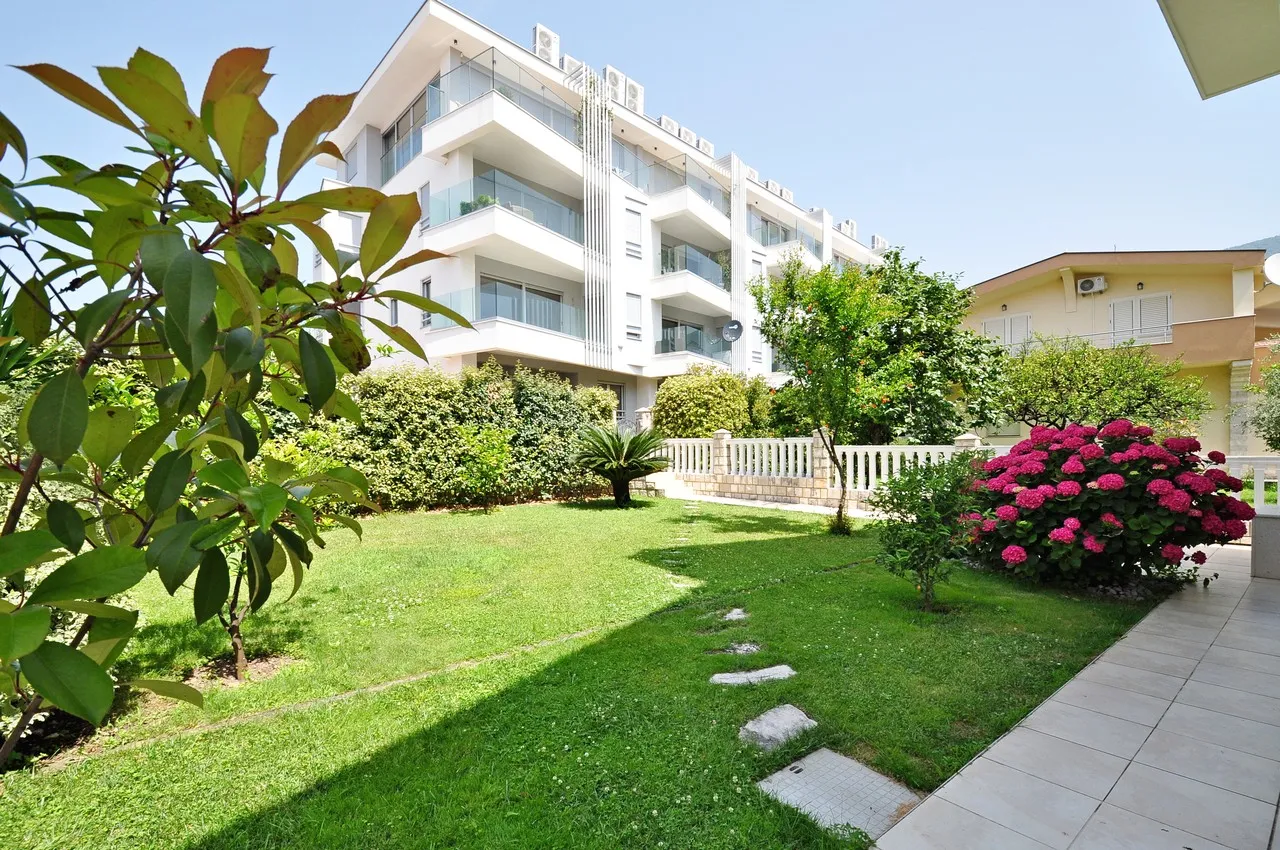 Green lawn garden with pink flowers and stepping stones leading to a white apartment building.
