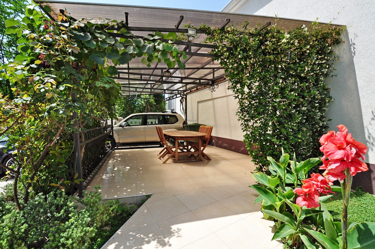 Cozy covered terrace with a wooden table and garden by the house in Tivat, Montenegro. Parking space in the yard.