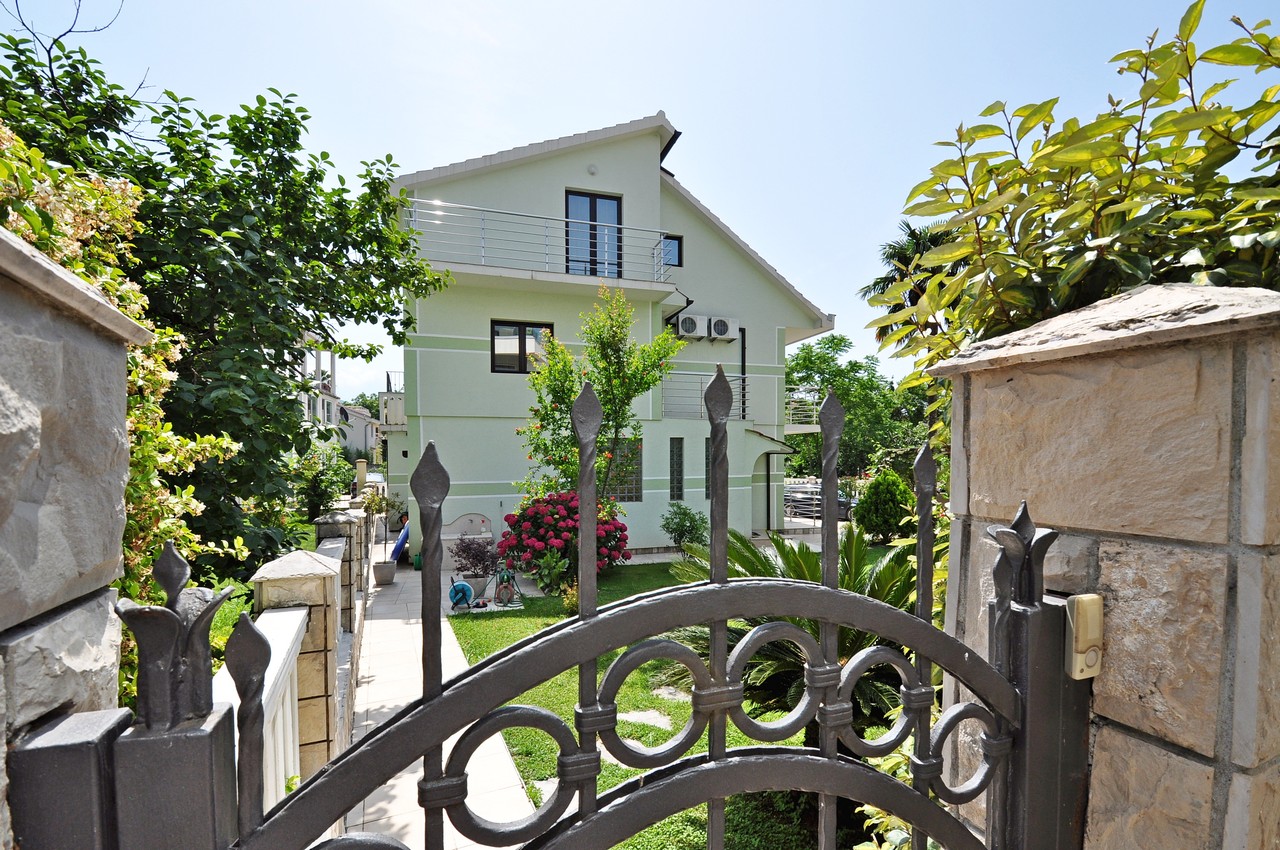 Three-story house with a garden and wrought-iron gates in Tivat, Montenegro, front view with terraces and a green plot.