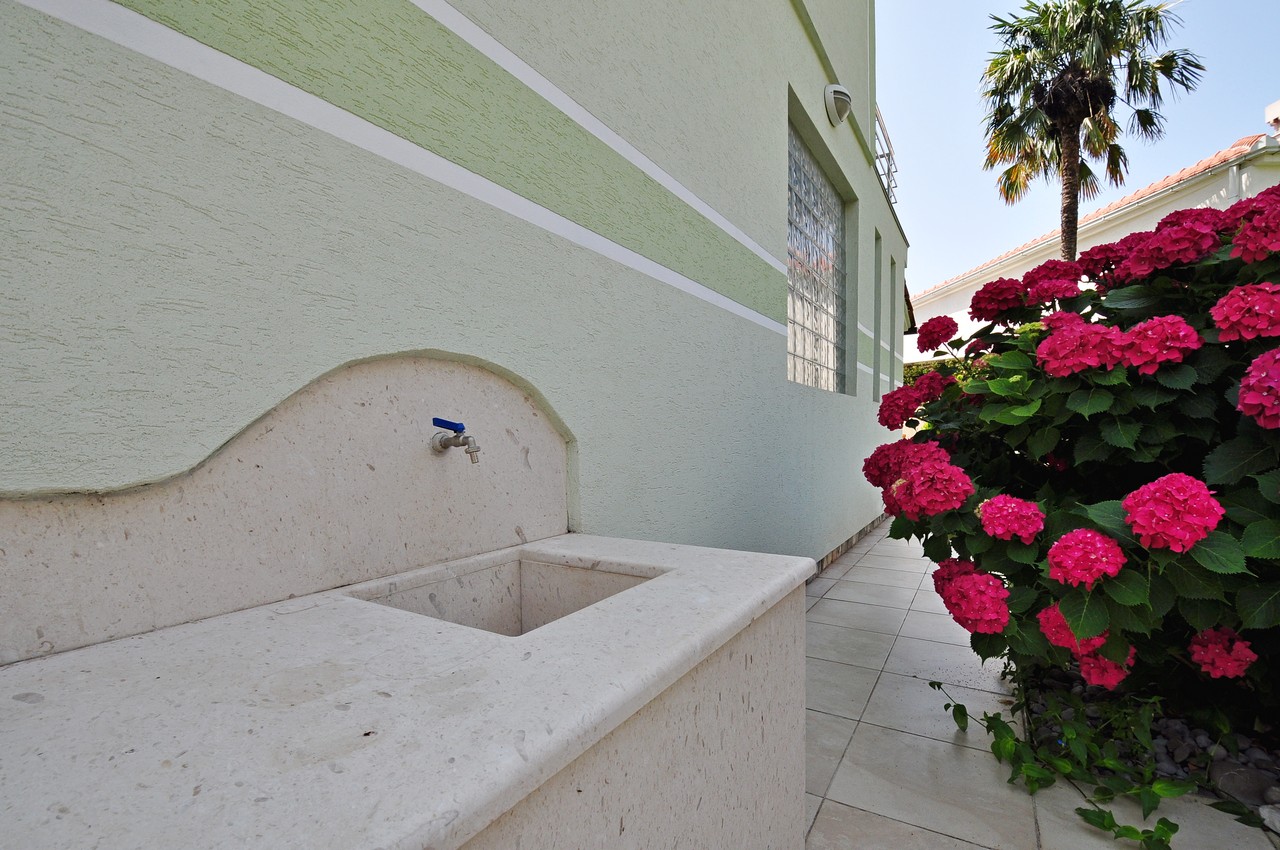Stone sink in the courtyard of a house in Tivat, Montenegro, near blooming hydrangeas and a palm tree on the property.