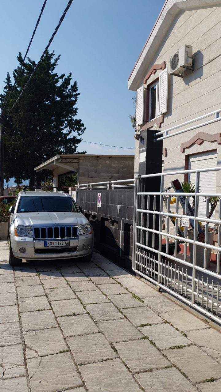 House facade in Tivat, Montenegro: private parking with metal gates and a stone-paved area.
