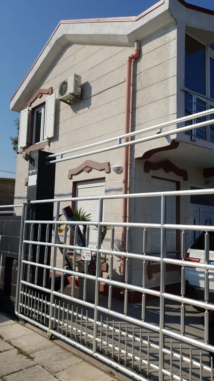 Exterior of a two-story house featuring a metal fence, air conditioner, and pink drainpipes on a light facade.