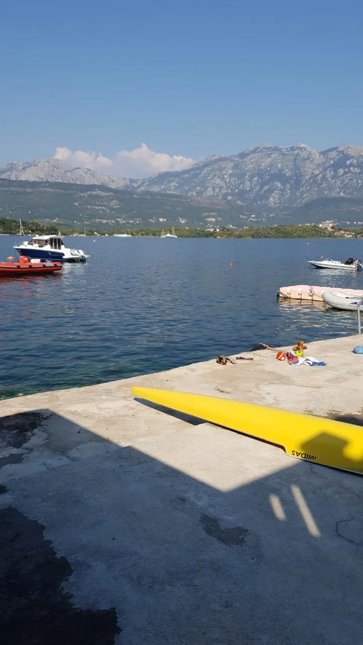 Concrete pier with a yellow kayak, boats on water, and mountains in the background. Outdoor scene.