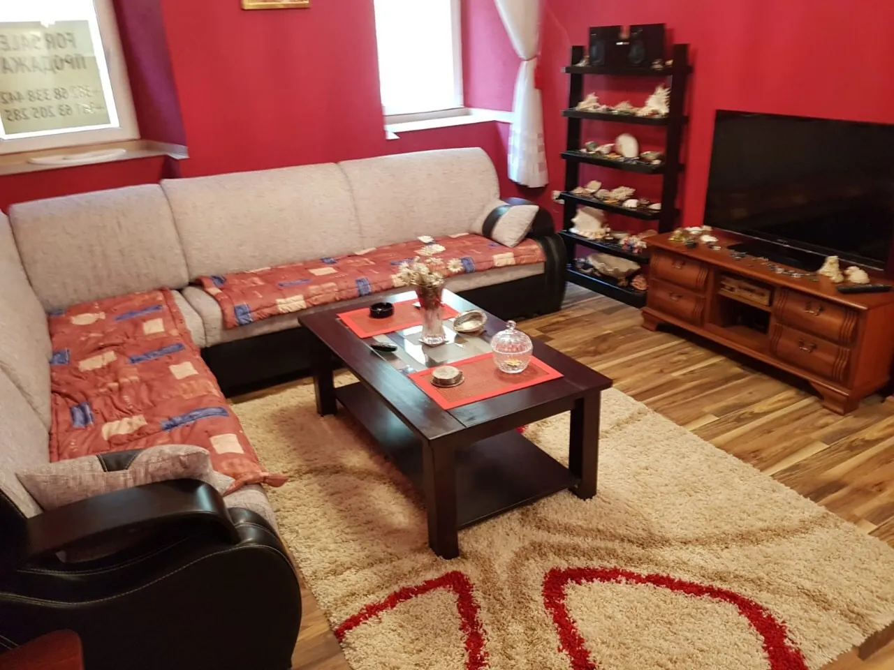 Living room with a corner sofa, coffee table, TV on a wooden stand, and red walls.