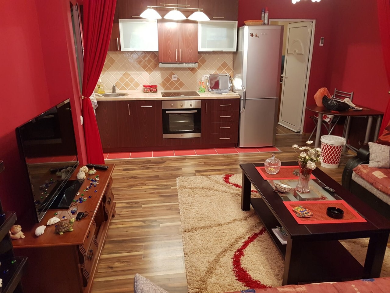 Living room with kitchen in an apartment in Budva, Montenegro: dark furniture, red walls, and a cozy rug.