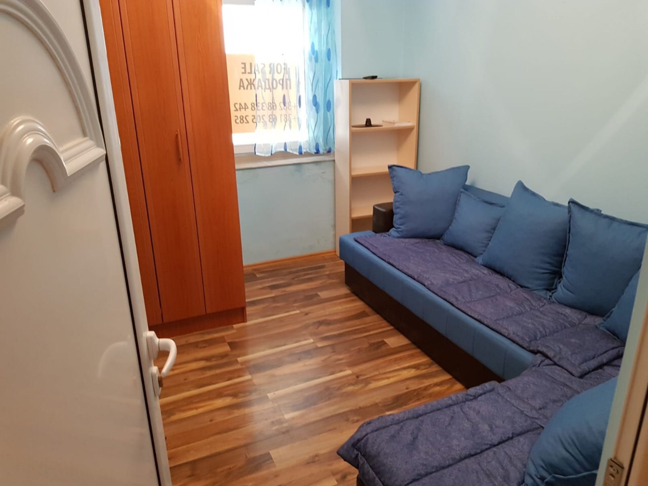 Living room in an apartment in Budva, Montenegro: blue corner sofa, wooden cabinet, shelving unit, and laminate flooring.