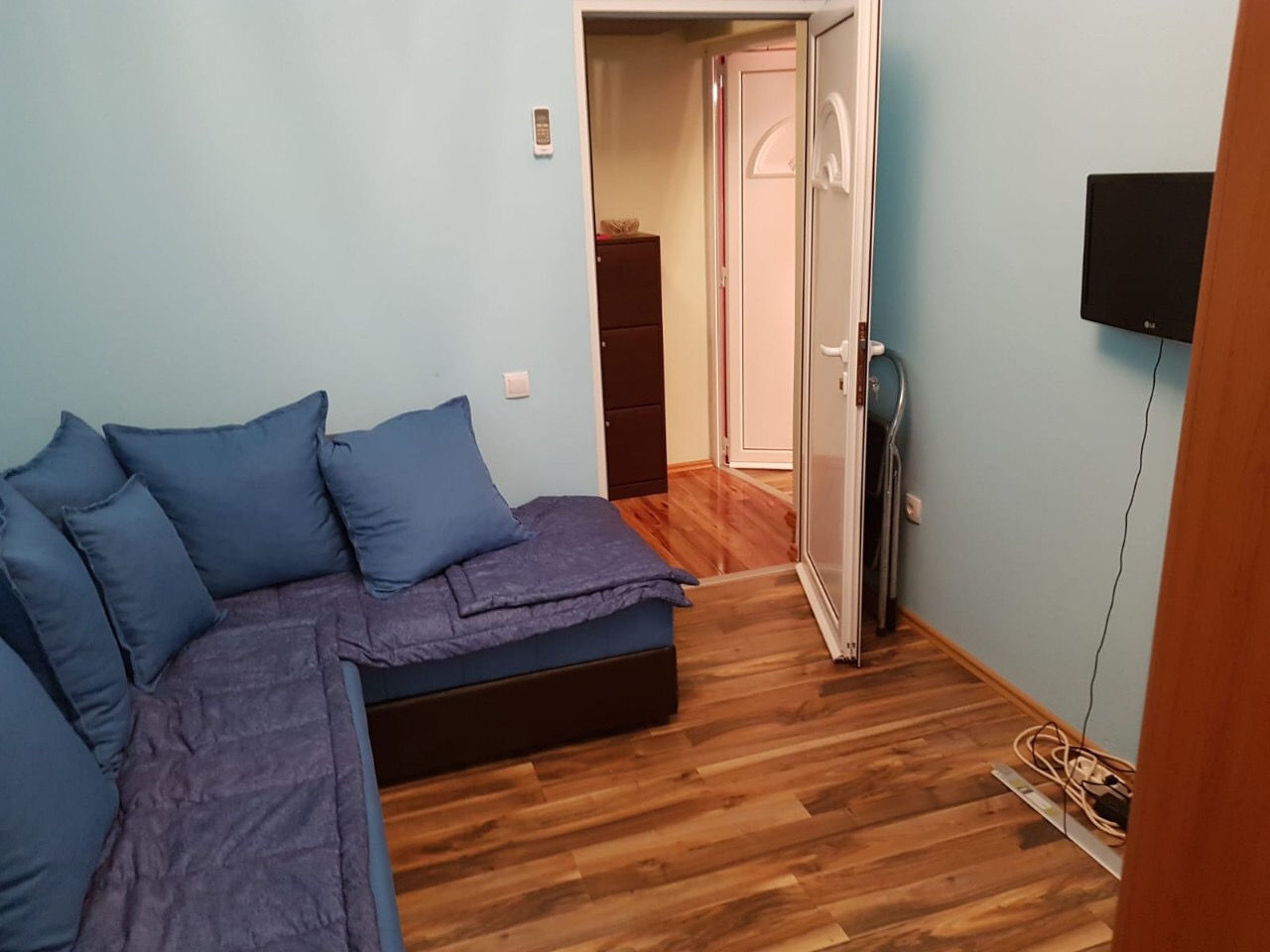 Living room with a blue corner sofa, laminate flooring, and a TV in an apartment for sale in Budva, Montenegro.