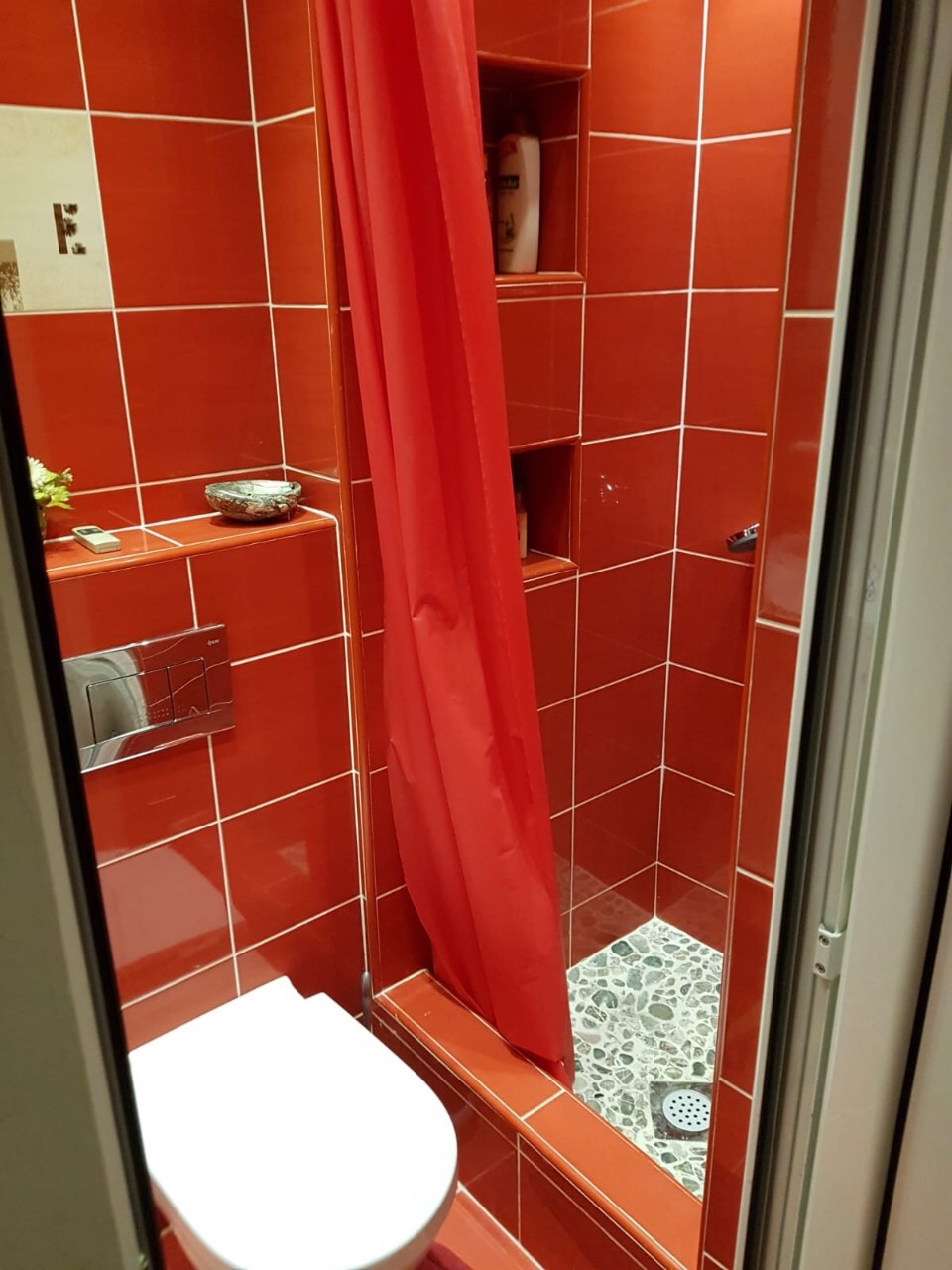Bathroom with red tiles, a shower cabin, and a wall-hung toilet in an apartment, Budva, Montenegro.