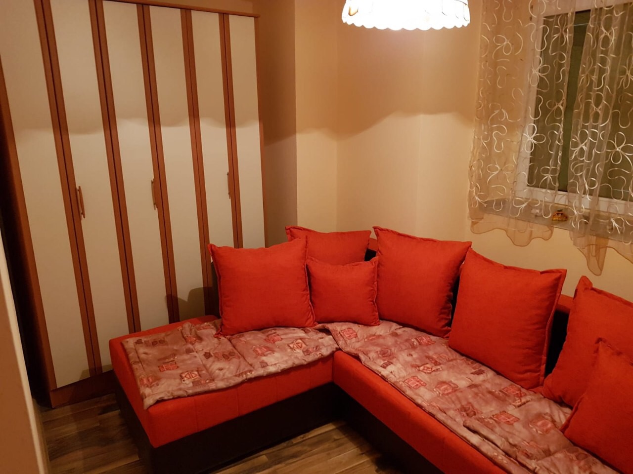 Cozy living room with a red corner sofa and a cabinet in an apartment in Budva, Montenegro. Interior with parquet flooring.