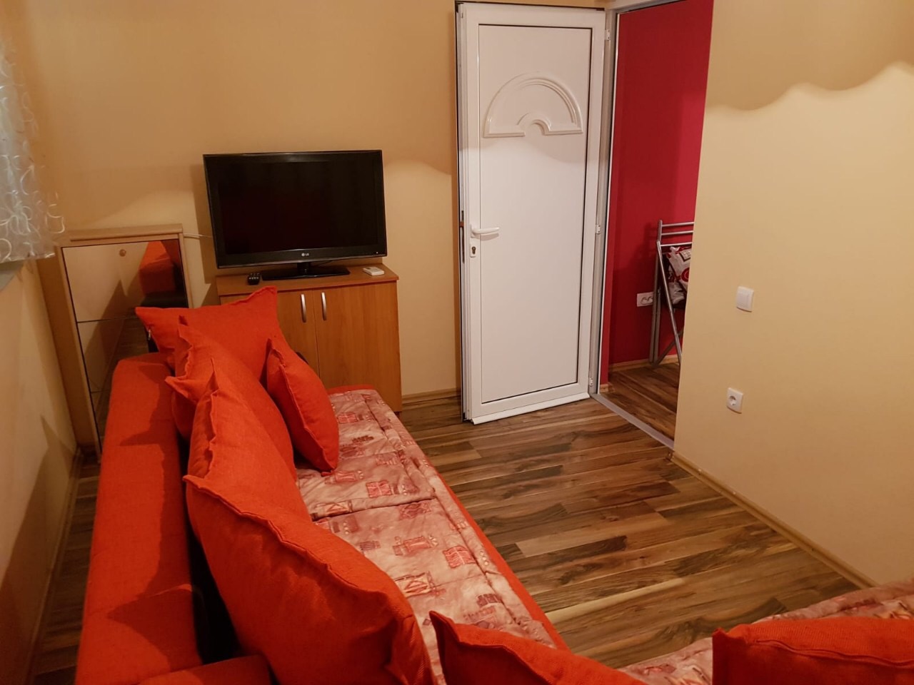 Living room with a red sofa, TV, and laminate flooring in an apartment for sale in Budva, Montenegro.