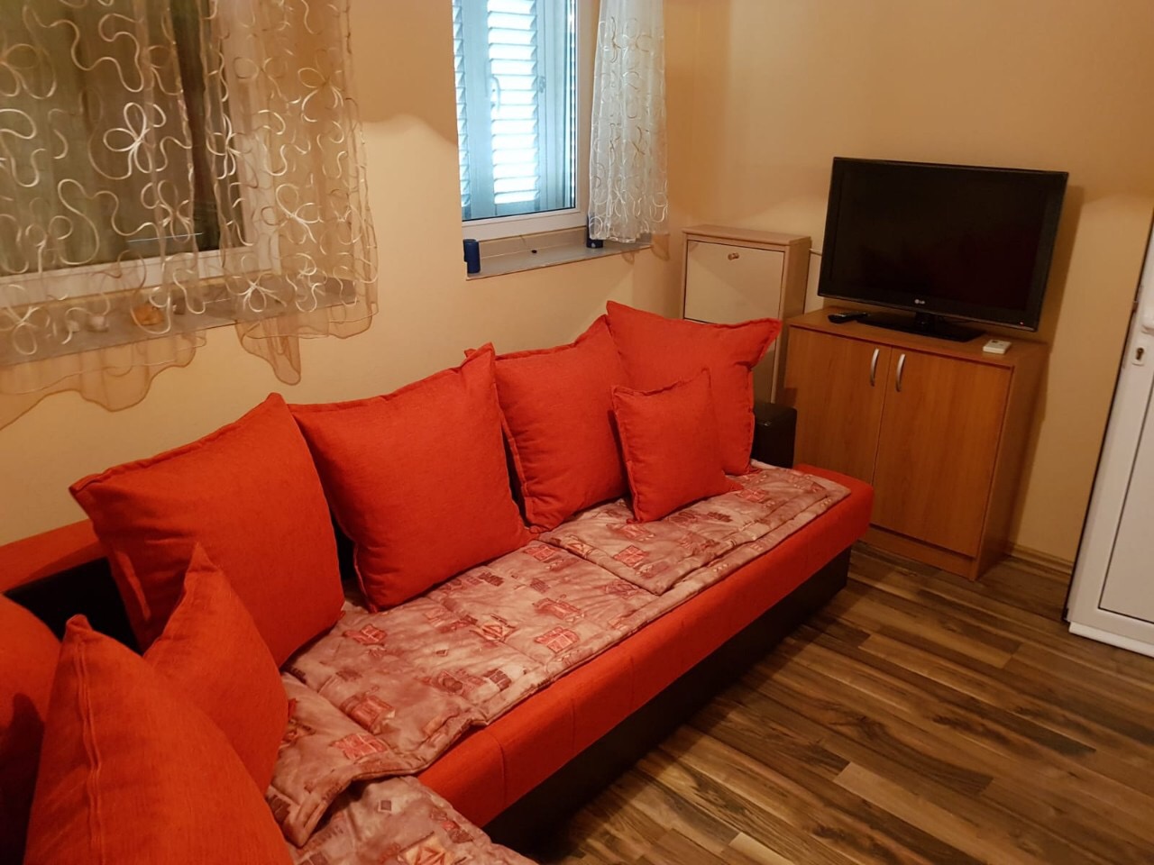 Cozy living room with a red sofa and TV in an apartment for sale in Budva, Montenegro. Interior with laminate flooring and a window.