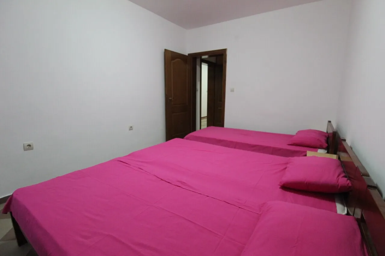 Two beds with bright pink bedding in a room with white walls and a wooden door leading out.