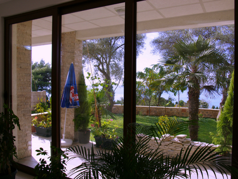 View from the living room onto the terrace and garden with palm trees in a house in Sutomore, Bar Riviera, Montenegro. Panoramic glazing.