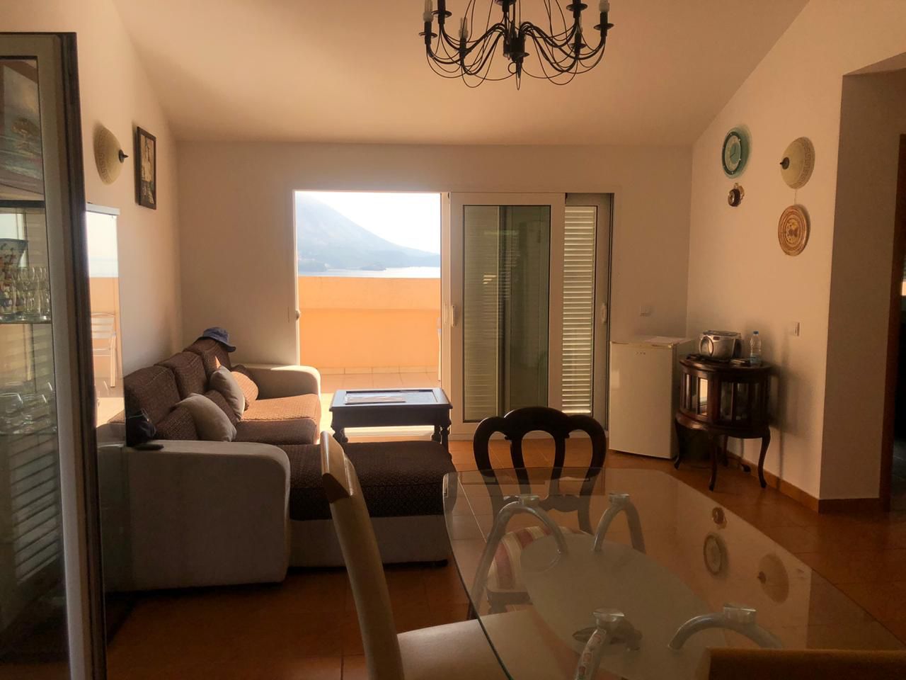 Living room in an apartment in Bečići, Montenegro: a soft sofa, a glass dining table, and access to a terrace with sea views.