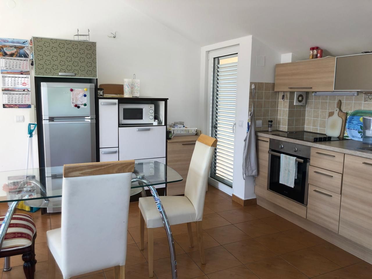 Bright kitchen in an apartment in Bečići, Montenegro: modern cabinetry, dining area with a glass table, and tiled flooring.