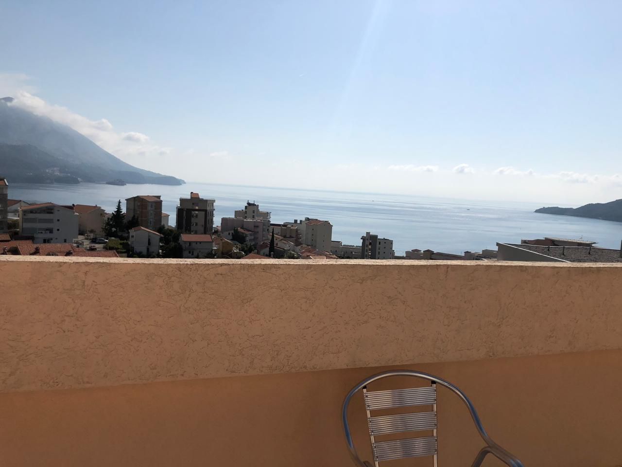 Sea and mountain view from the apartment balcony in Bečići, Montenegro: a panorama of the coast and metal garden furniture.