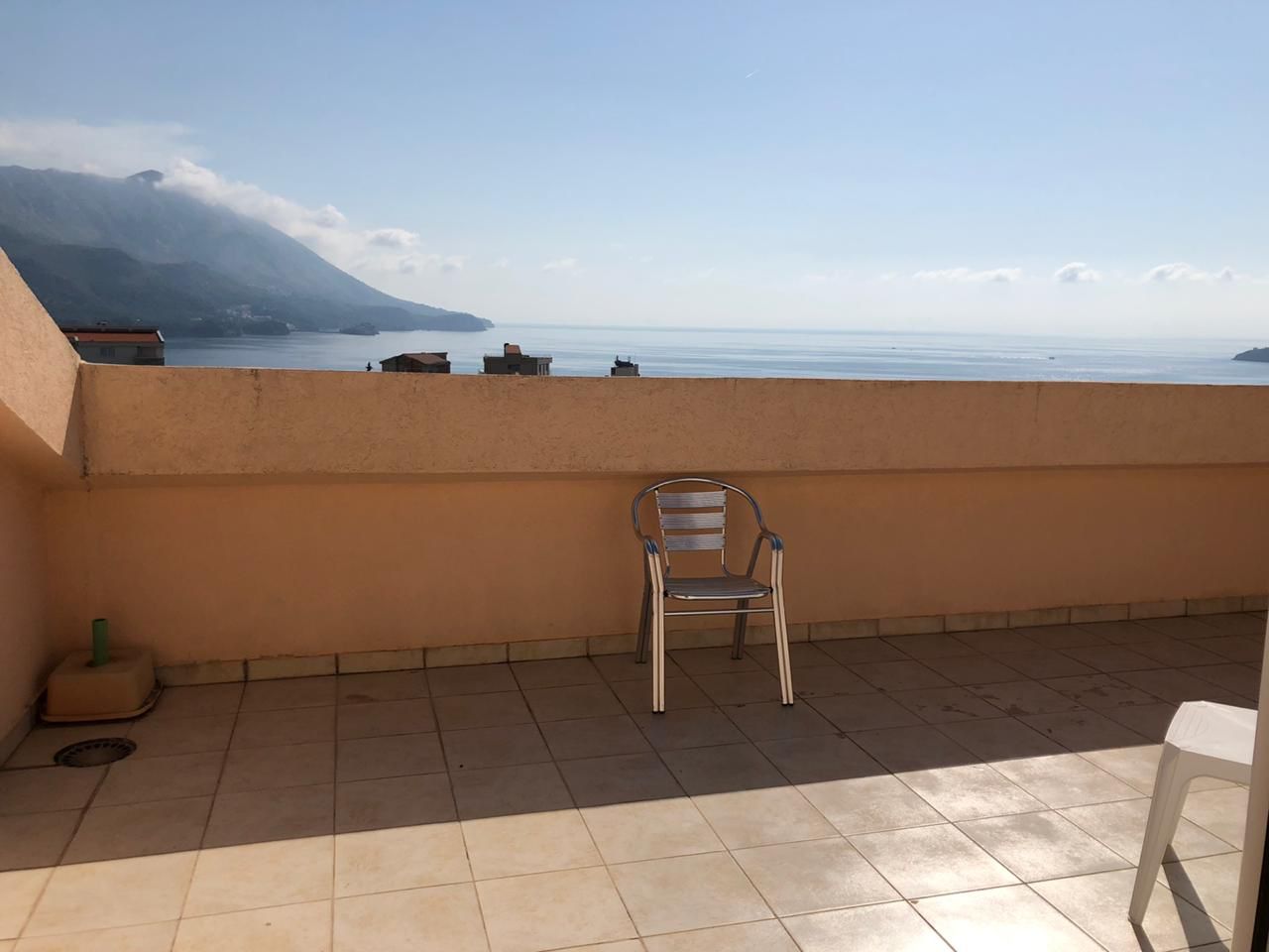 Apartment terrace in Bečići, Montenegro: sea and mountain view, tiled floor, metal chair, open balcony.