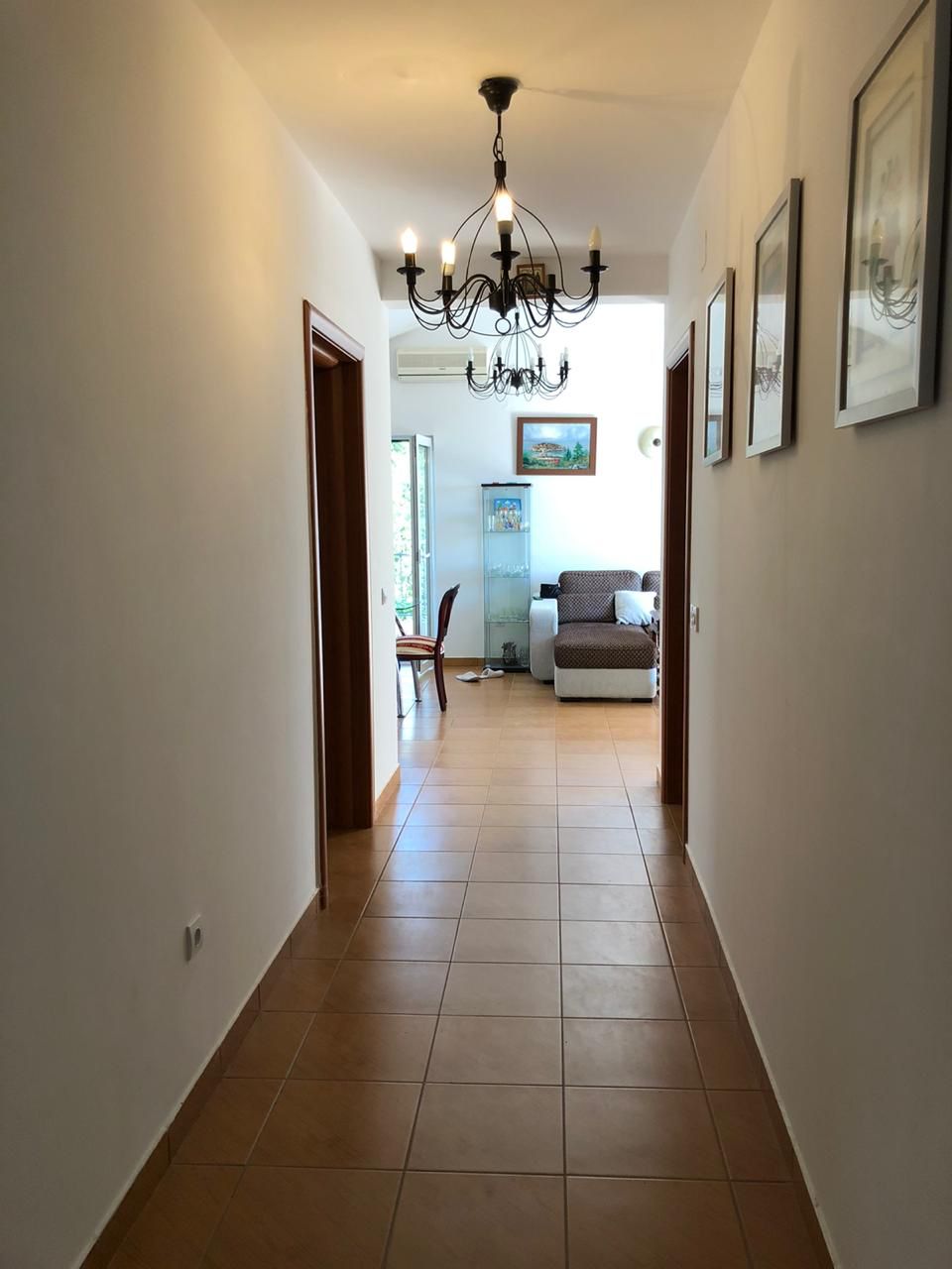Bright hallway with tile and a wrought-iron chandelier leading to the apartment living room in Becici, Montenegro.