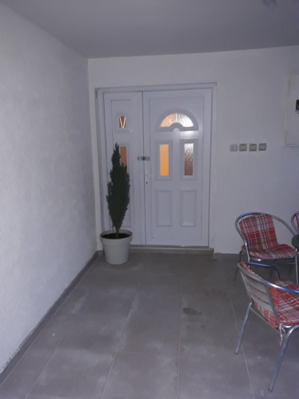 Entrance to the house in Zhanitsa, Montenegro: white double door, tiled terrace, chairs, and a decorative plant.