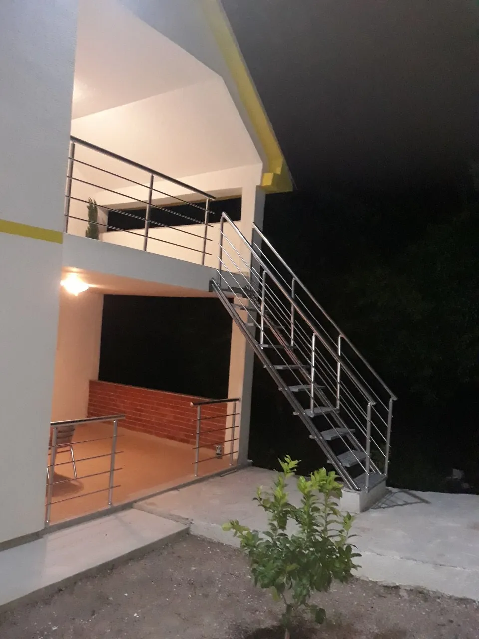 Night view of the house exterior featuring a metal staircase leading to an upper balcony and a lower terrace area.
