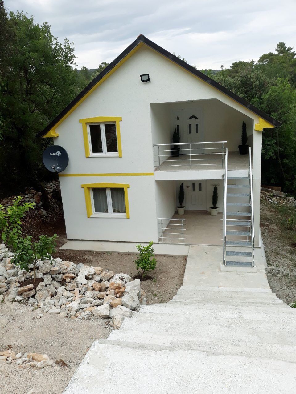 Two-story house with yellow trim and an exterior staircase in Zhanitsa, Montenegro: view of the facade and surrounding area.