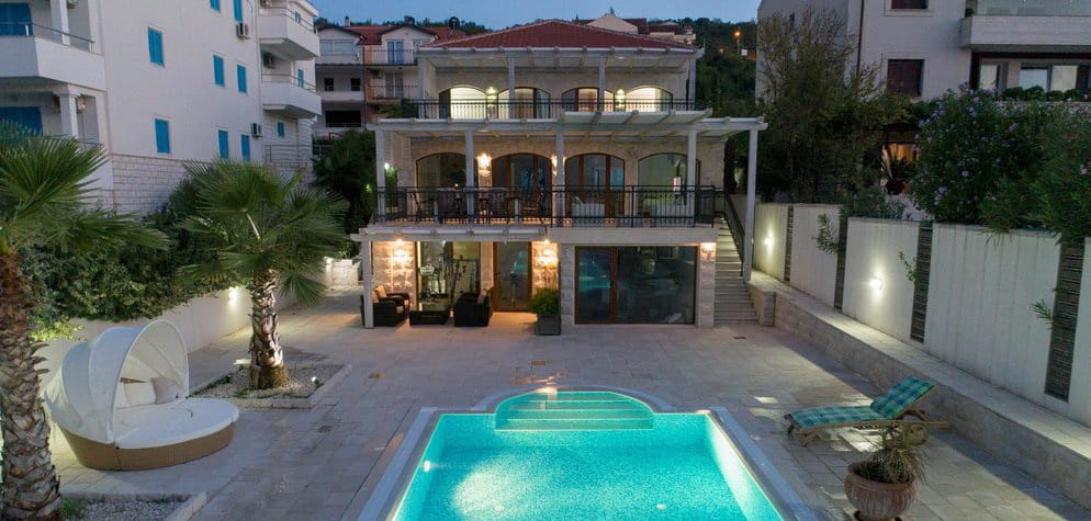 Two-story villa in Krašići, Montenegro: private pool, furnished terrace, palm trees, and landscape lighting in the evening.