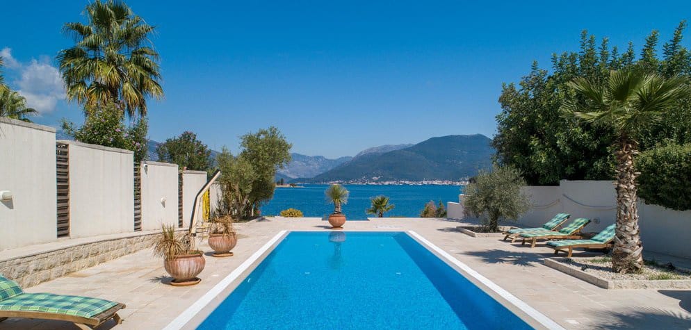 Pool at a villa in Krašići, Montenegro: terrace with sun loungers, palm trees, and panoramic views of the sea and mountains.